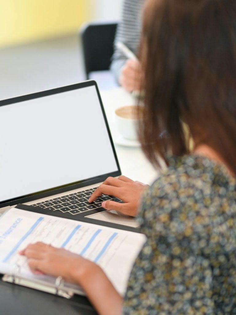 Verwaltungsaufgaben Person tippt auf einer Laptop-Tastatur, Notizen und eine Tasse im Hintergrund.
