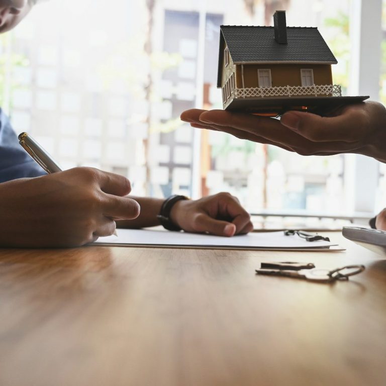 Wohnungsübergabe Hände übergeben ein Modellhaus, während jemand Notizen macht.